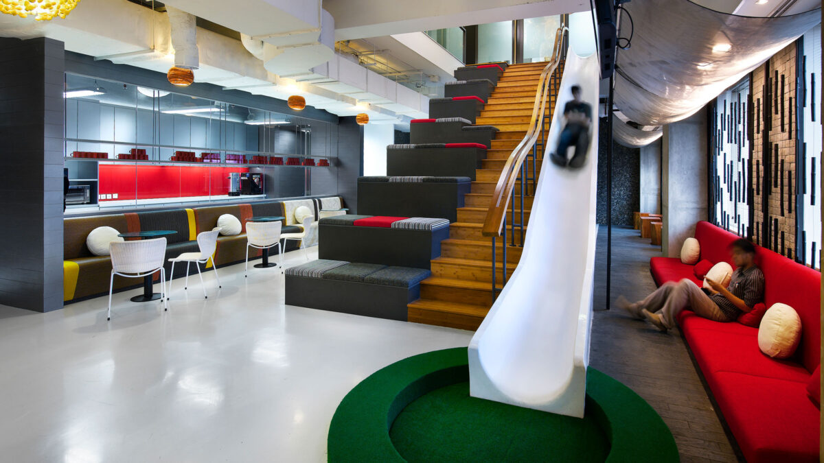 man going down slide and man sitting on long chair in casual breakout area