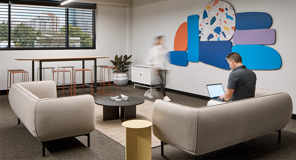 man working in casual seating area while woman walks by