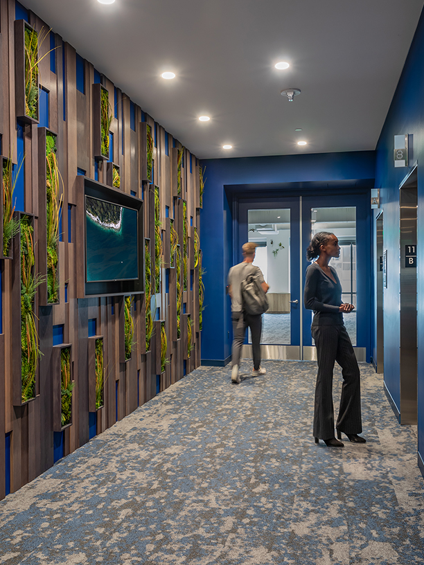 man walking in down corridor and woman waiting for lift
