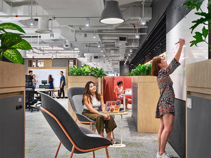 woman giving presentation to colleague, woman working in booth and group of people collaborating at the back