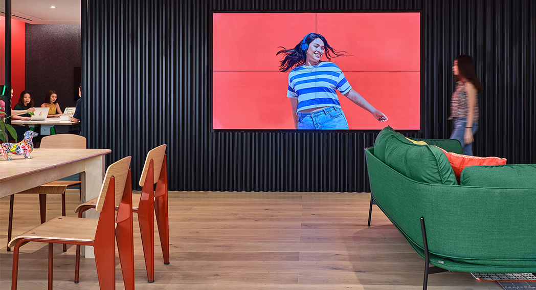 woman walking in front of av wall and people seen to be collaborating at back