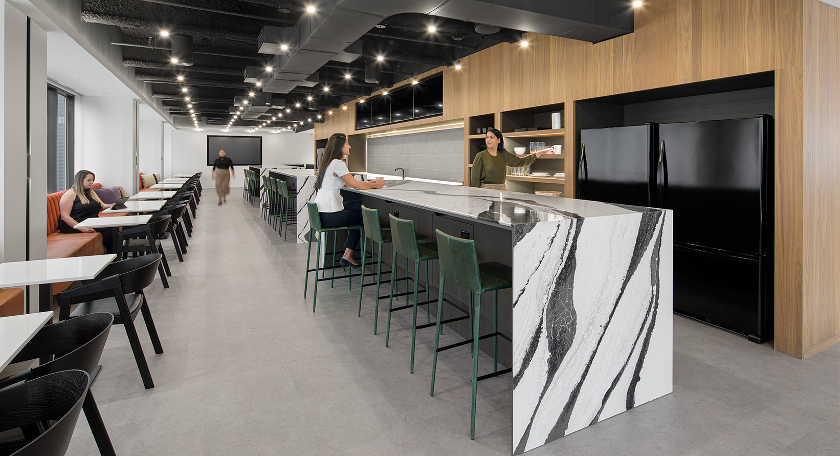 women talking by kitchen, woman sitting and working at table and woman walking