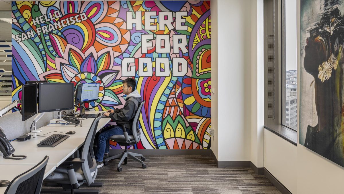 Custom artwork in modern San Francisco office by M Moser featuring Standard Chartered slogan Here for Good with individual workspaces, desks, office technology and ergonomic office chairs.