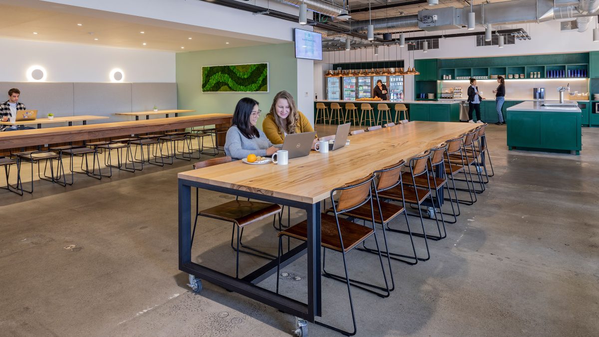The best office layout for collaboration featuring a hospitality-driven design with long family-style tables and banquet seating.
