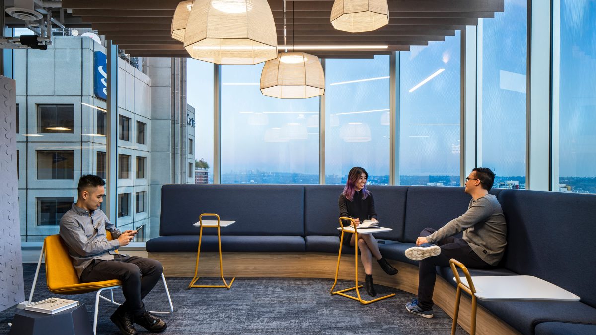 A workplace social hub featuring plush, wrap-around bench seating, small worktables and beautiful views of the Vancouver skyline and mountains.