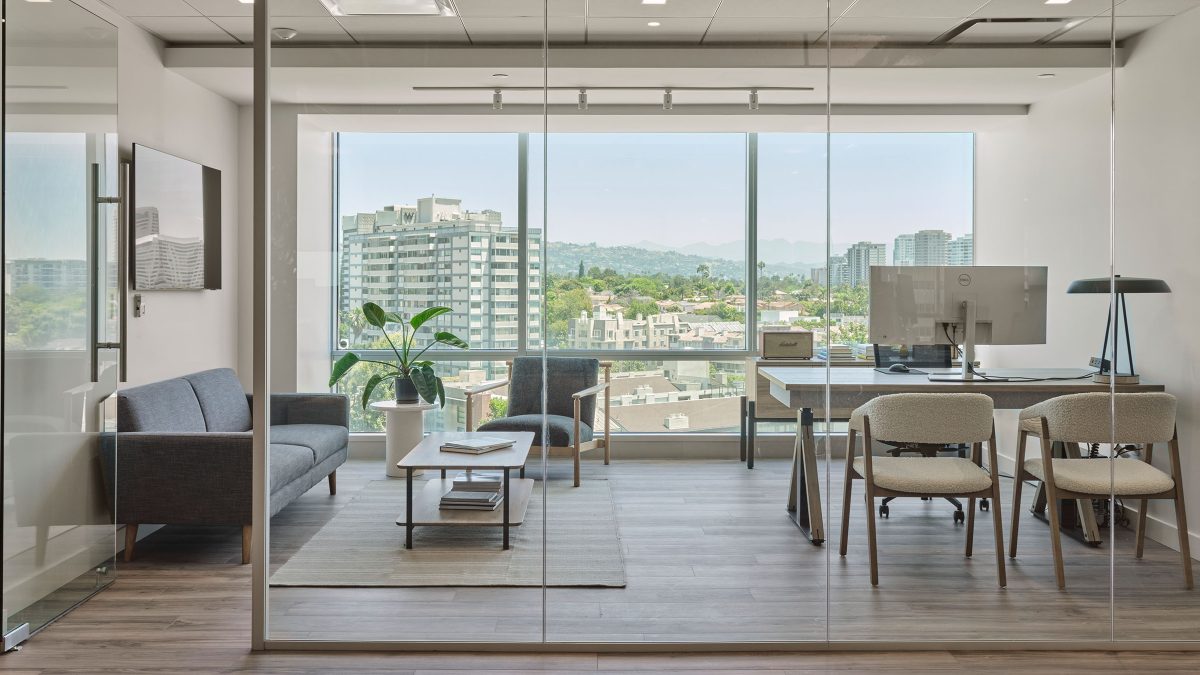 Interior office design featuring a private office filled with natural light, casual seating for meetings, technology and artwork.