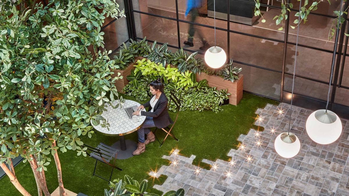 Corporate office interior design featuring unique work setting filled with greenery, live plants and outdoor furniture in an indoor environment.