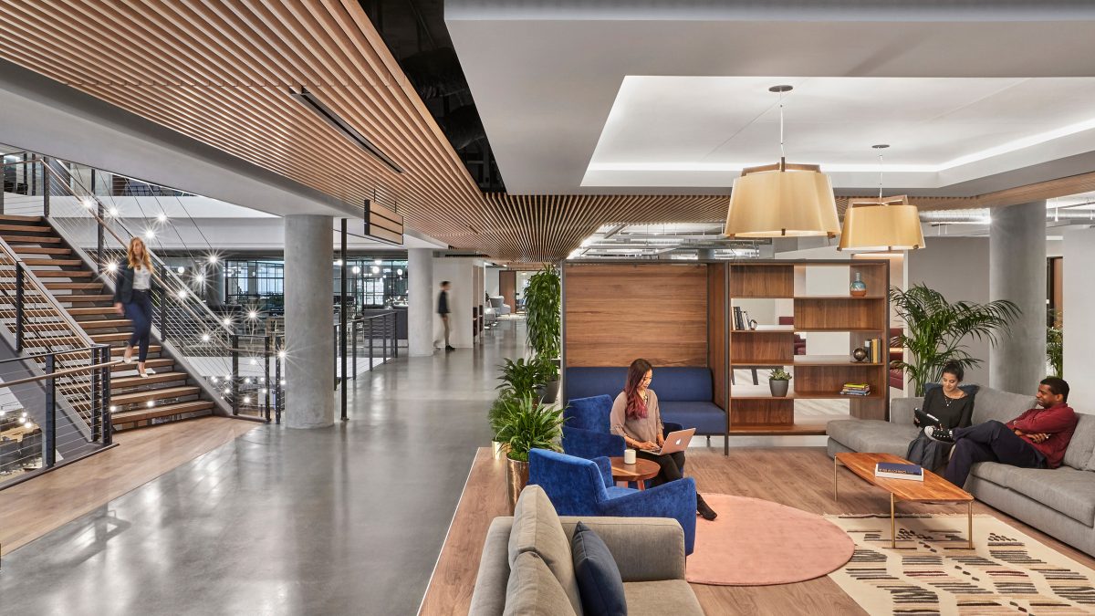 people working in a comfortable lounge setting, next to someone walking down a staircase