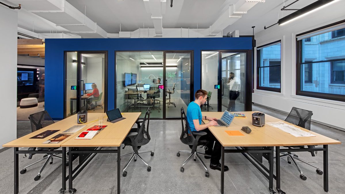 man working at desk and people in meeting rooms