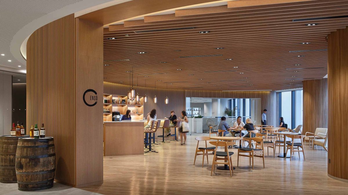 Interior view of a kitchen tasting room designed by M Moser, featuring curved walls and wood paneling on the ceiling. People are seated at the bar and tables, enjoying the space.