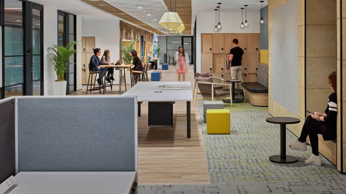 people collaborating in breakout area, man by lockers, woman in corridor and woman in booth